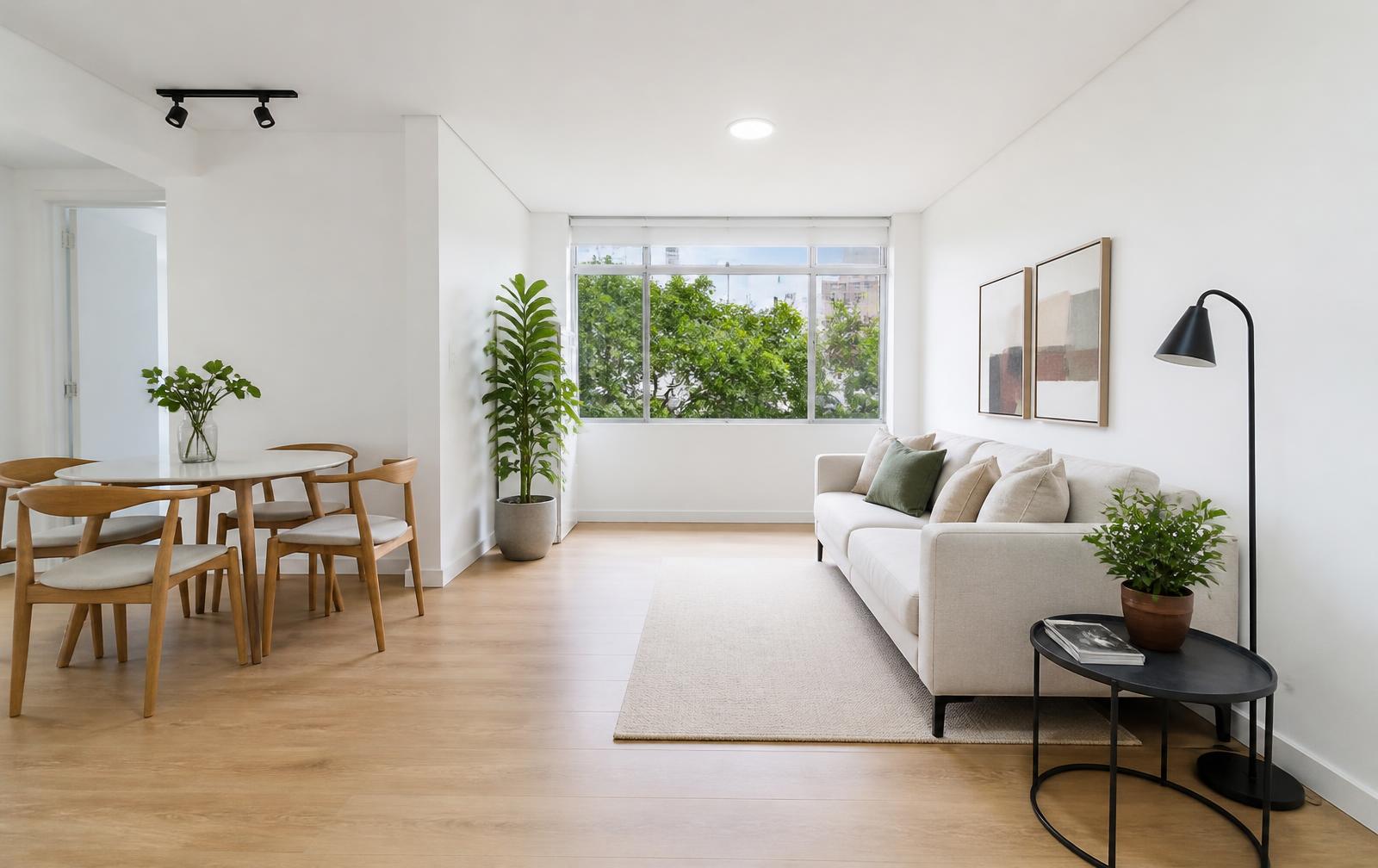 Sala de apartamento recém-reformada com paredes brancas e piso de madeira clara